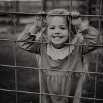 Photography of little girl poking face through the fence